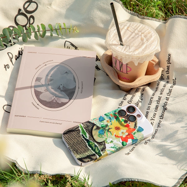 Book, phone with floral case, and cup on a blanket outdoors
