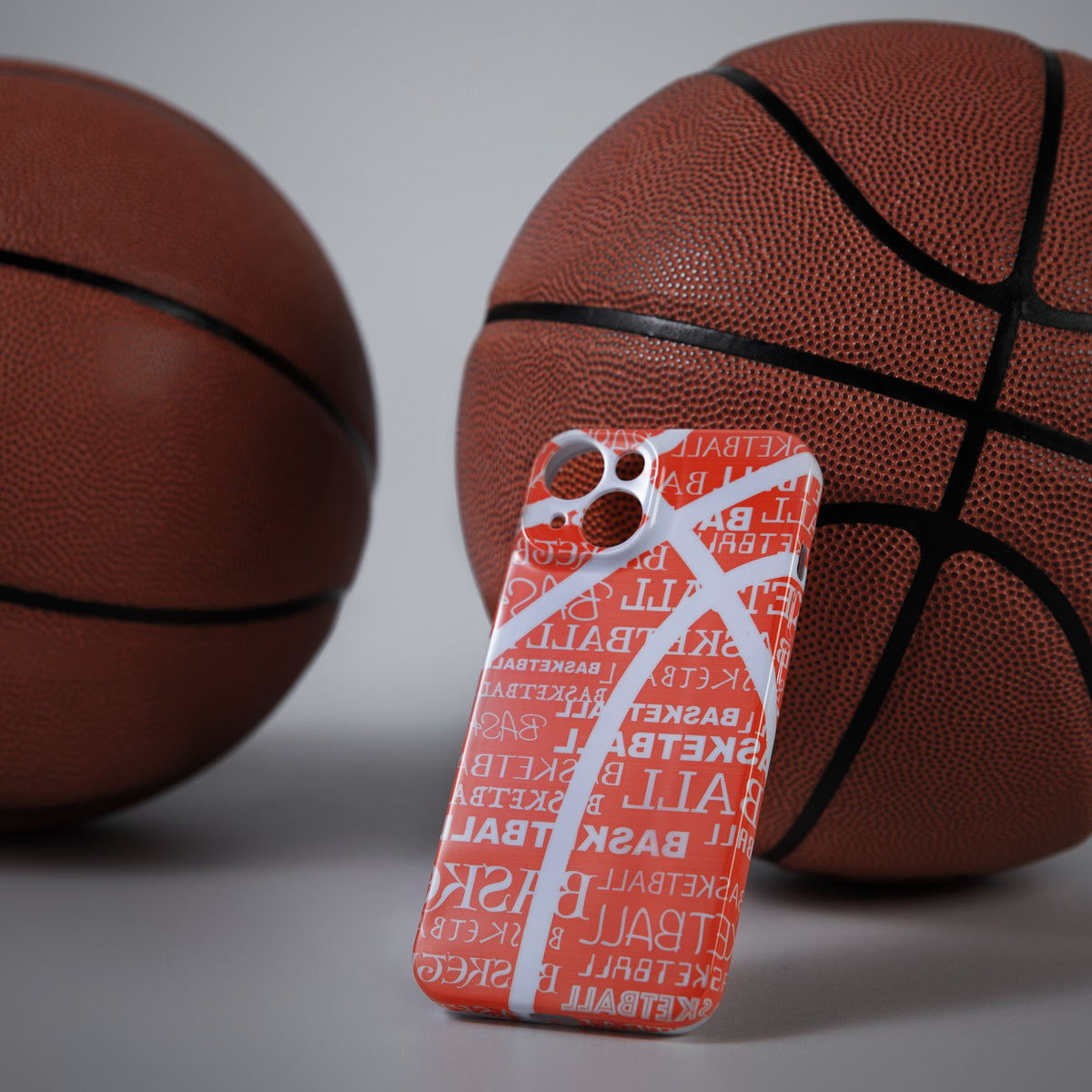 Phone case with basketball design in front of two basketballs on a light background