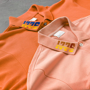 Two polo shirts, one orange and one pink, with visible brand labels on a gray surface.