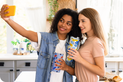 Two women taking a selfie in a kitchen holding drinks.