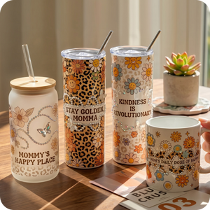 Set of decorative tumblers and mugs with various designs and text on a wooden surface.