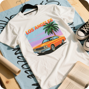 White t-shirt with a colorful 'Los Angeles' graphic featuring a palm tree and orange car, placed on a light blue surface with text.